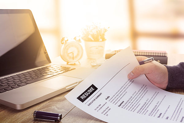 Hand holding resume in front of a laptop