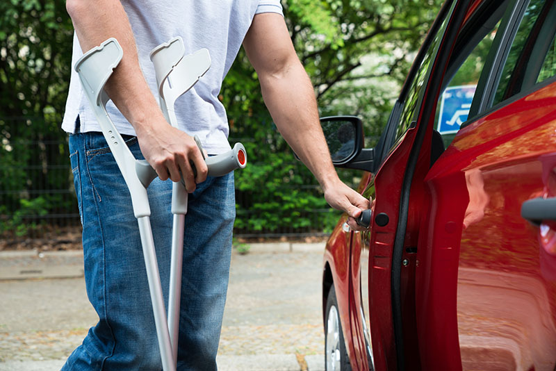 Man with crutches opening car door