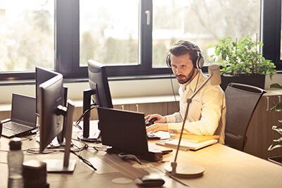 main wearing headphones sitting at a desk with computers