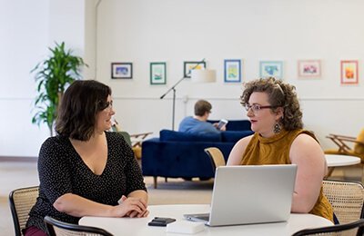 Two women talking at a desk with laptop