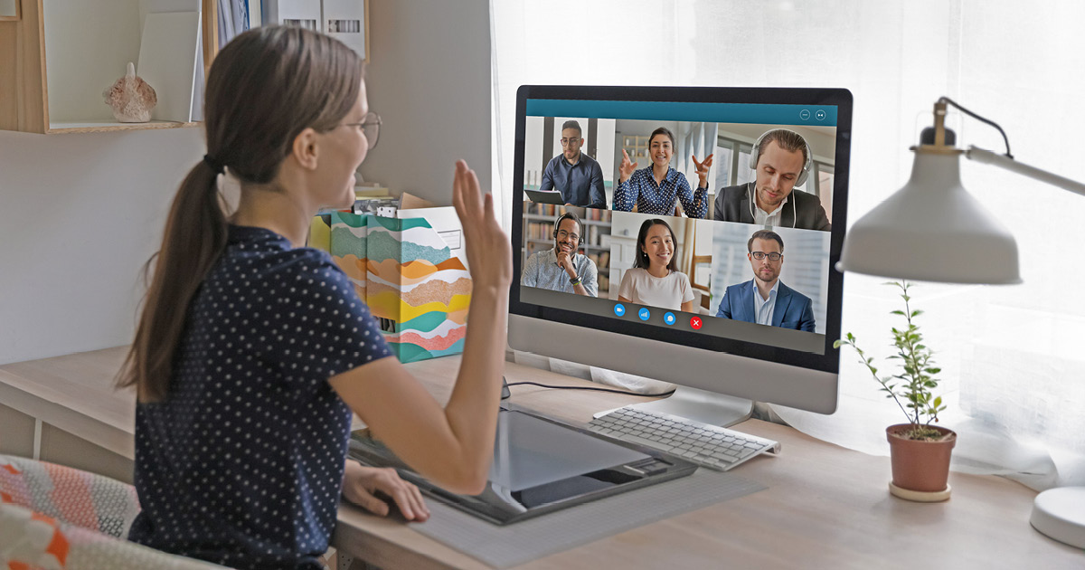 A person is attending a virtual meeting, waving at their laptop screen.